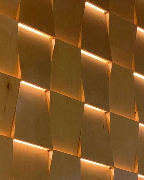 A wall of faceted oak panels with light washing out of the joints between them.