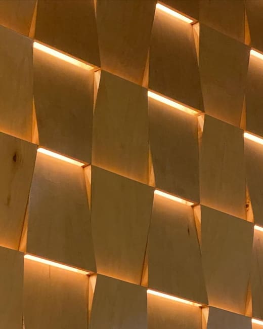 A wall of faceted oak panels with light washing out of the joints between them.