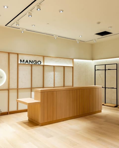 A pale oak reception counter and slatted wall paneling inside a Mango store.