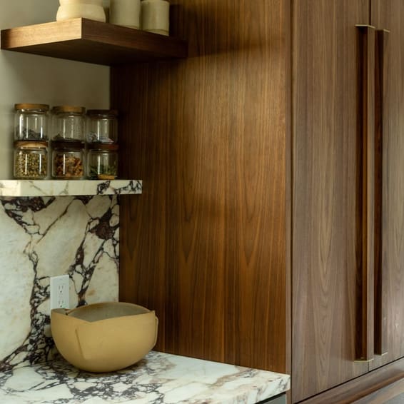 Walnut cabinetry beside a Calacatta Viola niche holding a brass bowl and glass jars.
