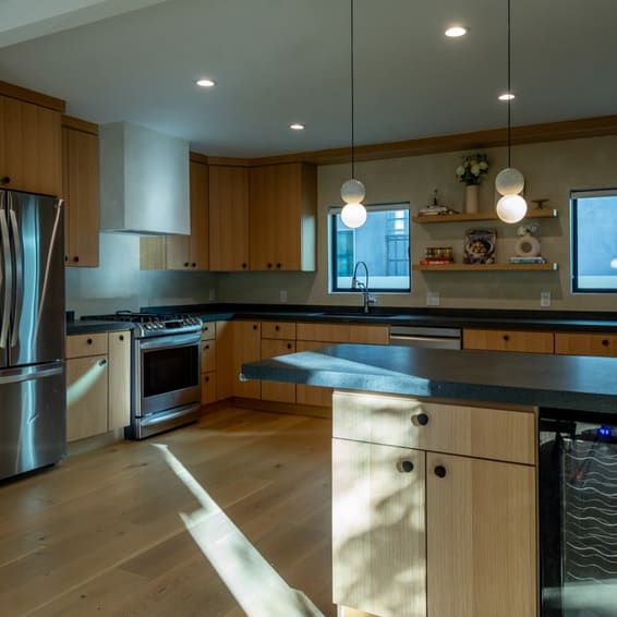 A white oak kitchen with dark stone counters and a long island, sunlight falling across the floor.