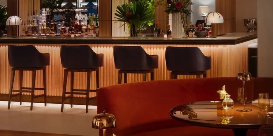 A hotel bar with fluted wood facing, dark stools and a curved red banquette.