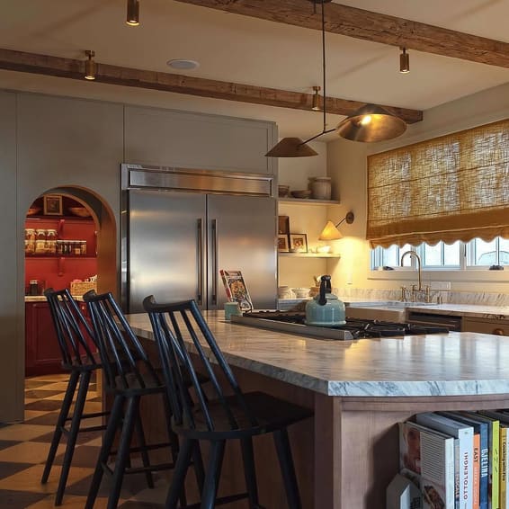 A kitchen island with black stools, a beamed ceiling and an arch through to the next room.