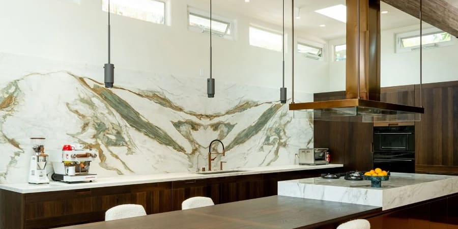 A walnut kitchen with a book-matched stone backsplash, suspended hood and a long island.