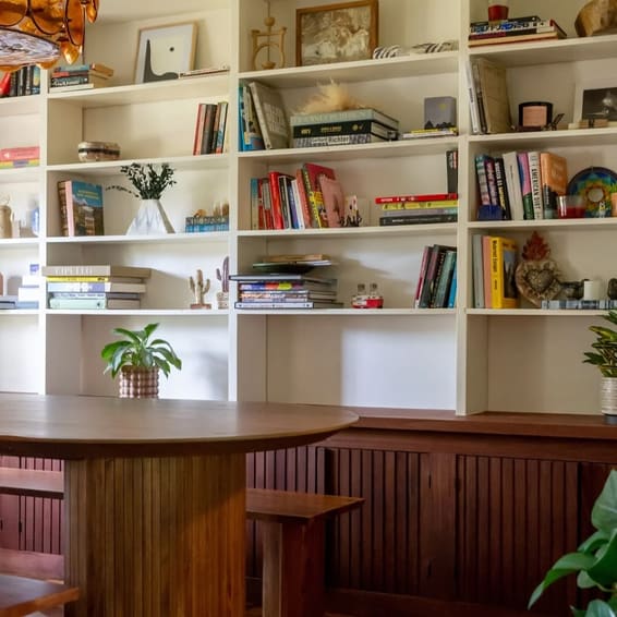 Floor to ceiling white built-in shelving above a fluted wood banquette and a round table.